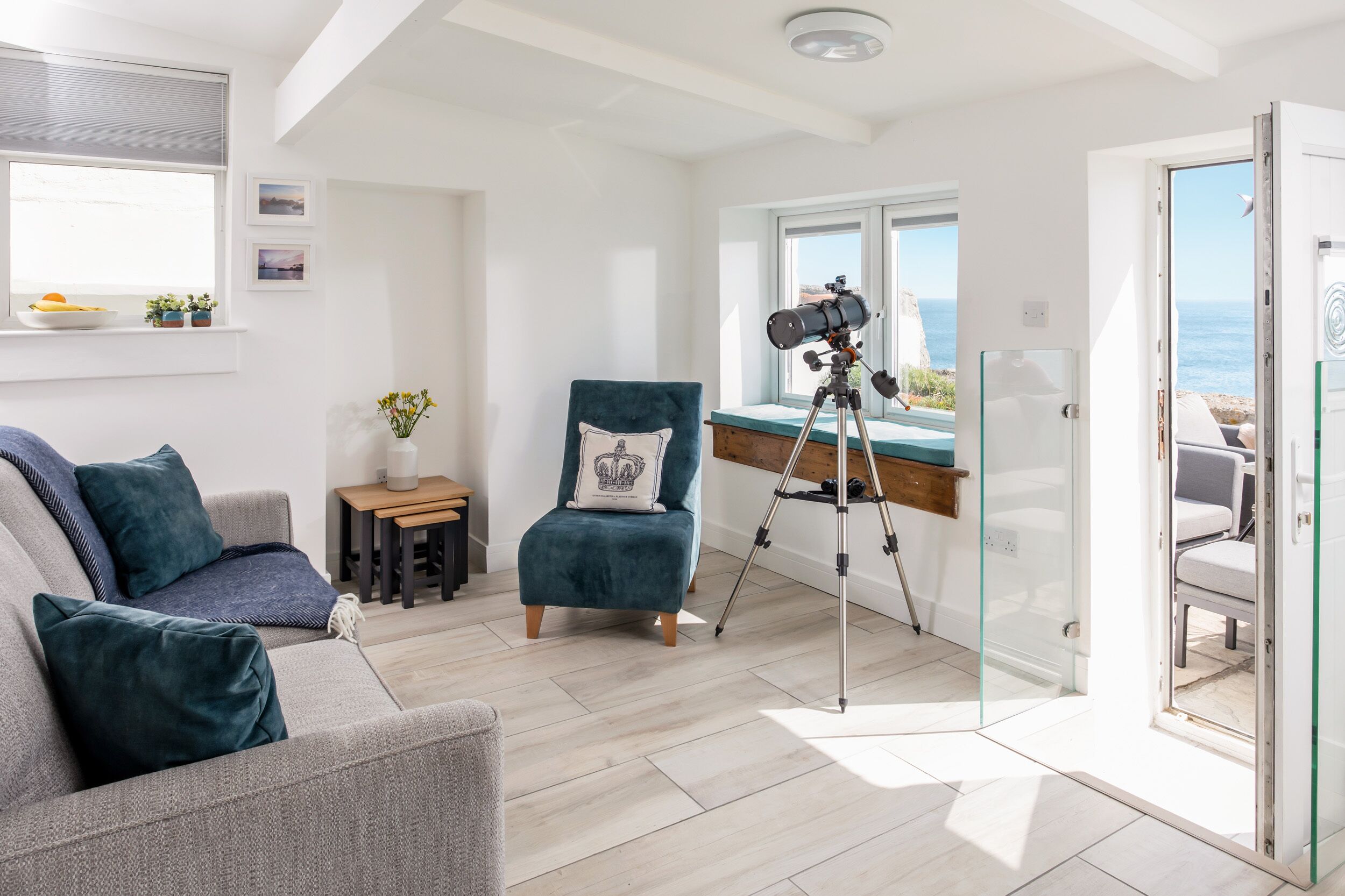 Une pièce moderne avec un canapé gris, un fauteuil turquoise et un télescope monté sur un trépied.
