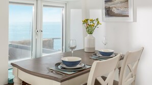 A dining area with a view of the sea, a vase with flowers, and a framed picture on the wall. - Loe Cottage (Helston)