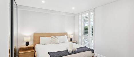 Une chambre moderne avec un lit, des tables de chevet et une fenêtre avec des stores.