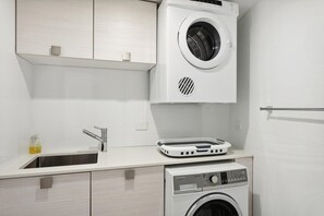 A compact laundry area with a front-loading washing machine, a dryer, and a sink.