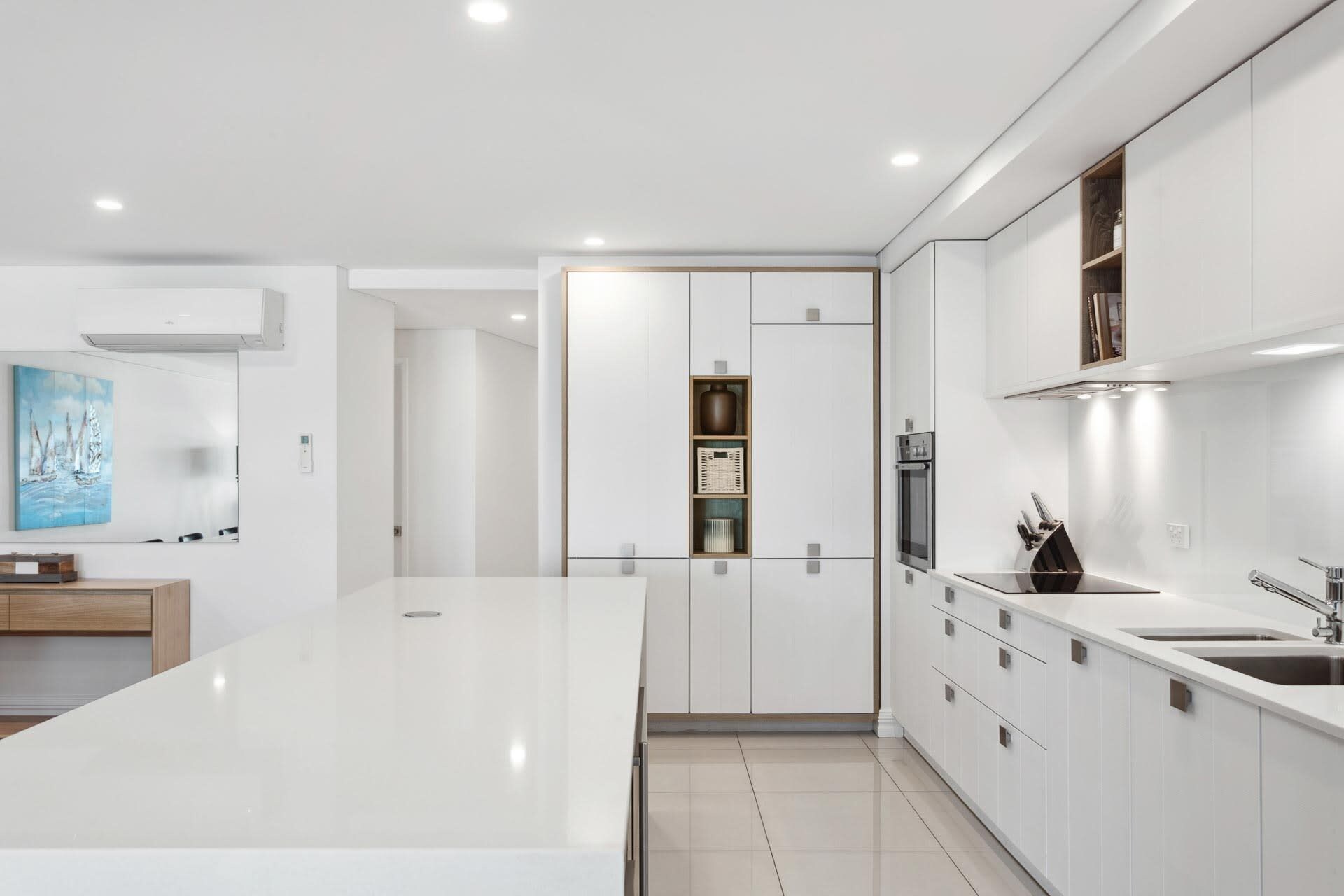 A modern kitchen with white cabinetry, a central island, and built-in appliances.