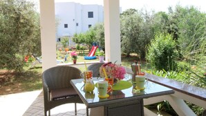 An outdoor patio with wicker chairs and a glass table, overlooking a garden with a slide and play area. - Apartments Danijela Novalja (Novalja)