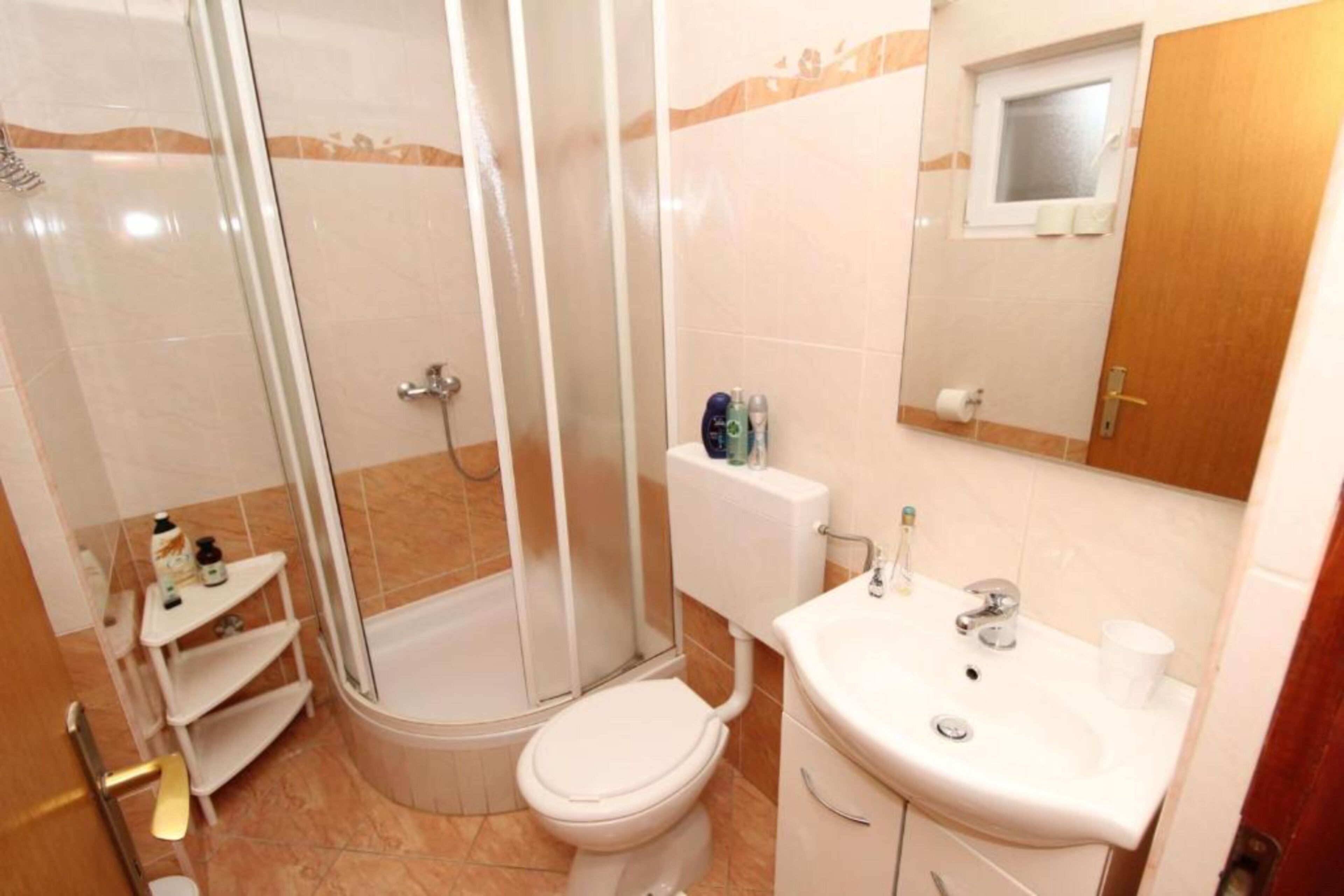 A bathroom with a shower, toilet, sink, and a small shelf with toiletries.