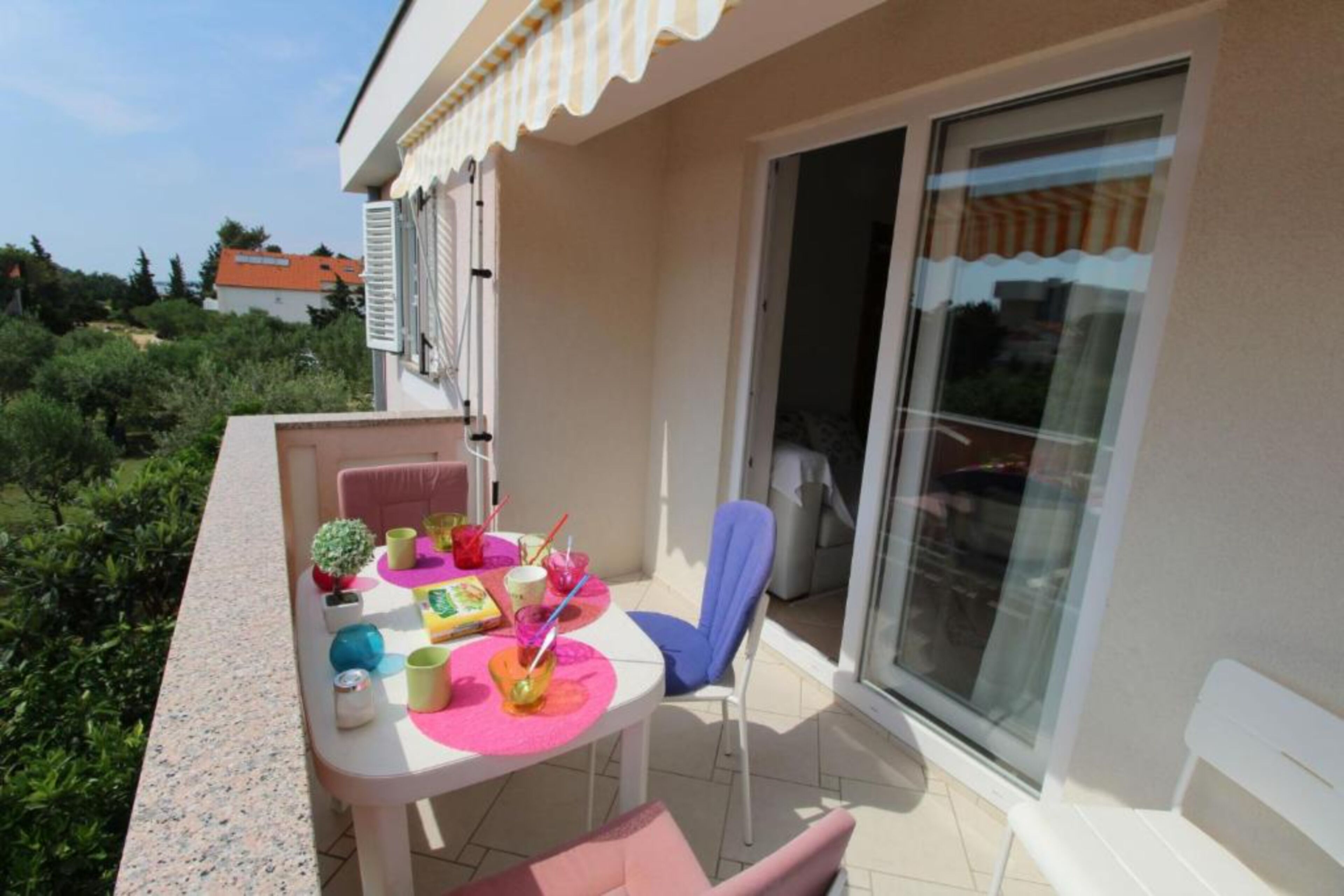 A balcony with a table set for a meal, a chair, and a glass door leading to a covered area.