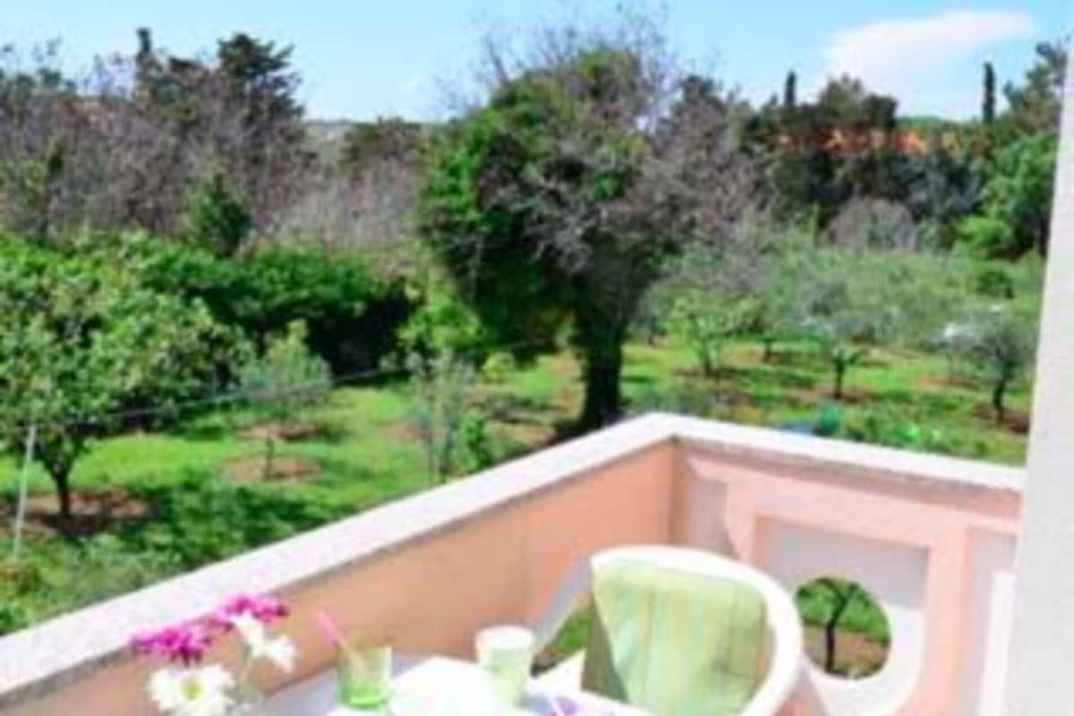 Un balcon avec une table dressée pour le dîner, entouré de chaises, donnant sur un jardin où l’on peut admirer divers arbres et arbustes.