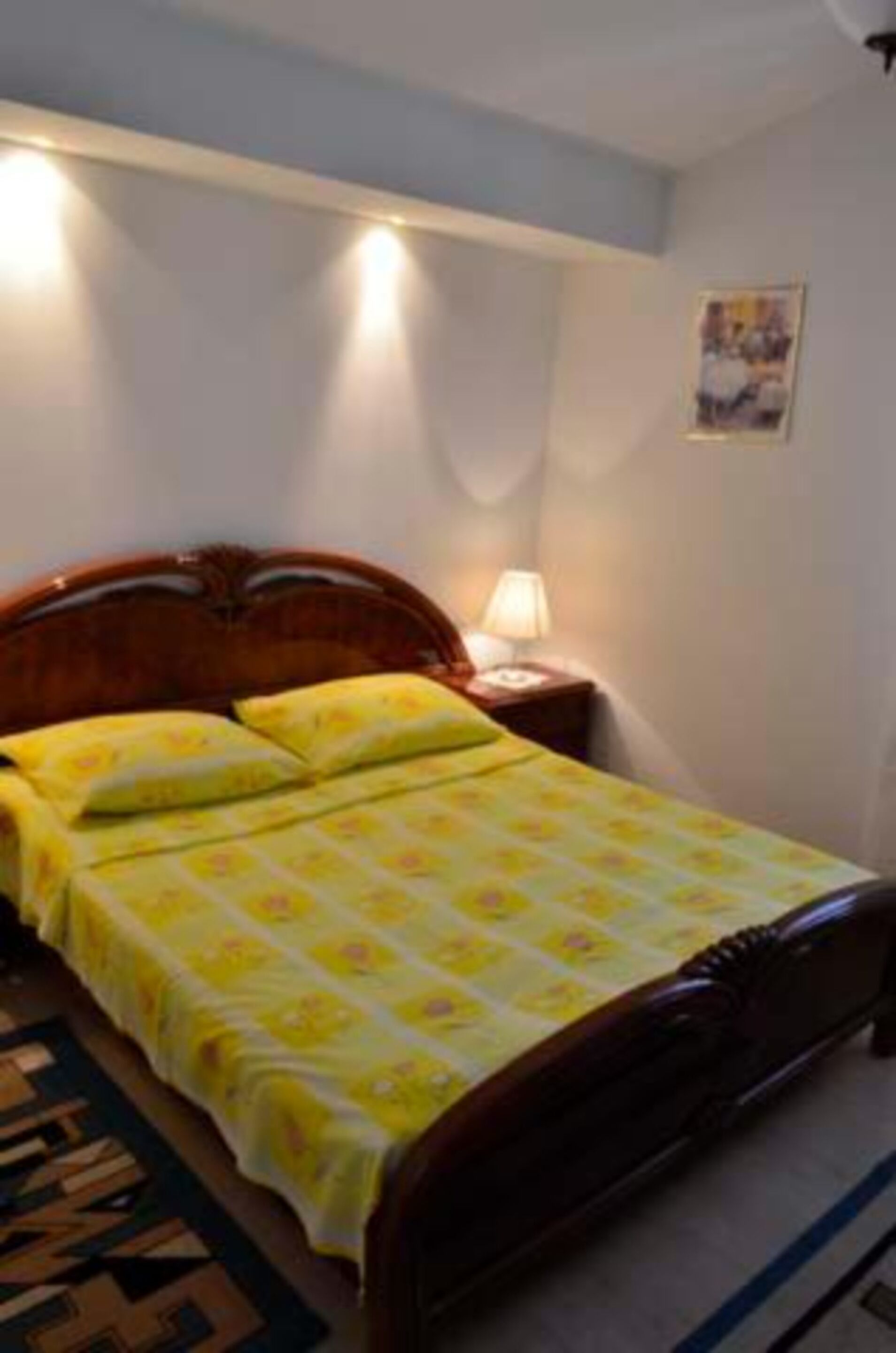 A single bed with a wooden headboard, a yellow floral bedspread, and a bedside lamp.