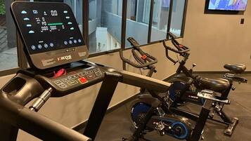 A gym with cardio machines, a digital display, and a TV on the wall.