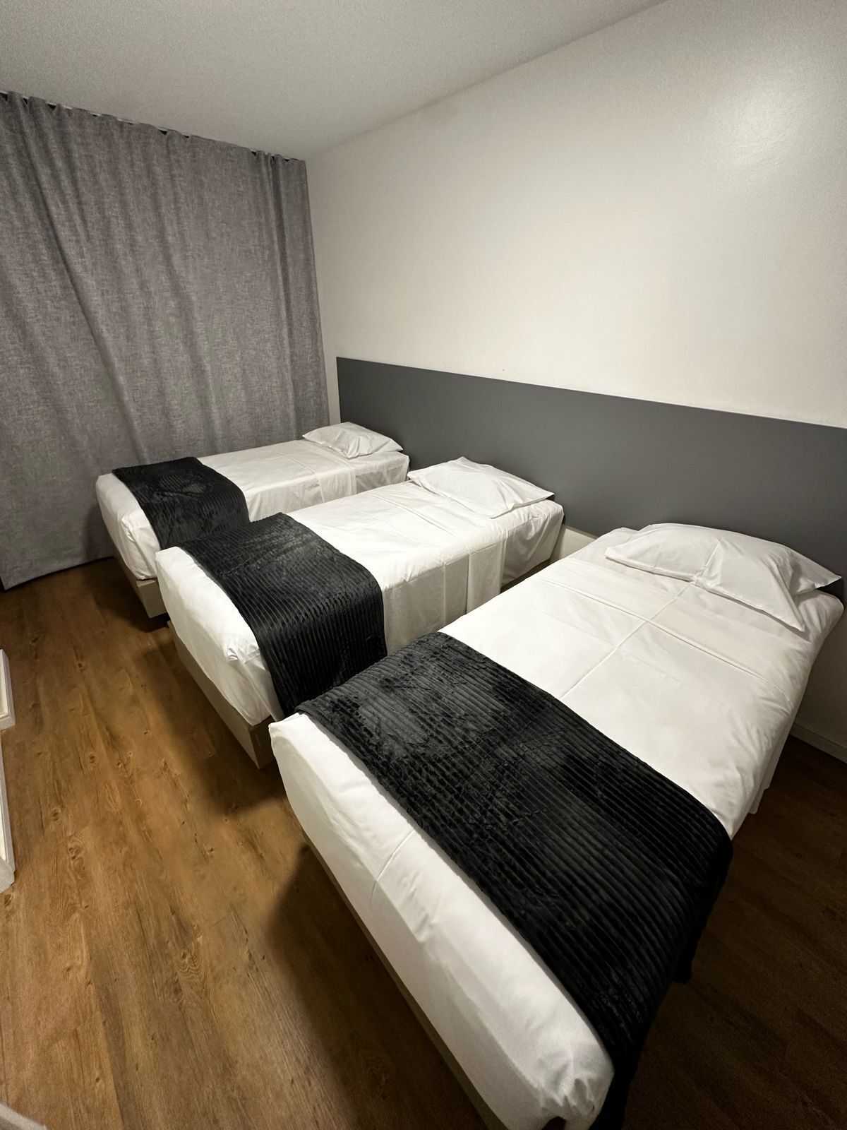 A hotel room with two single beds, a grey curtain, and a wooden floor.