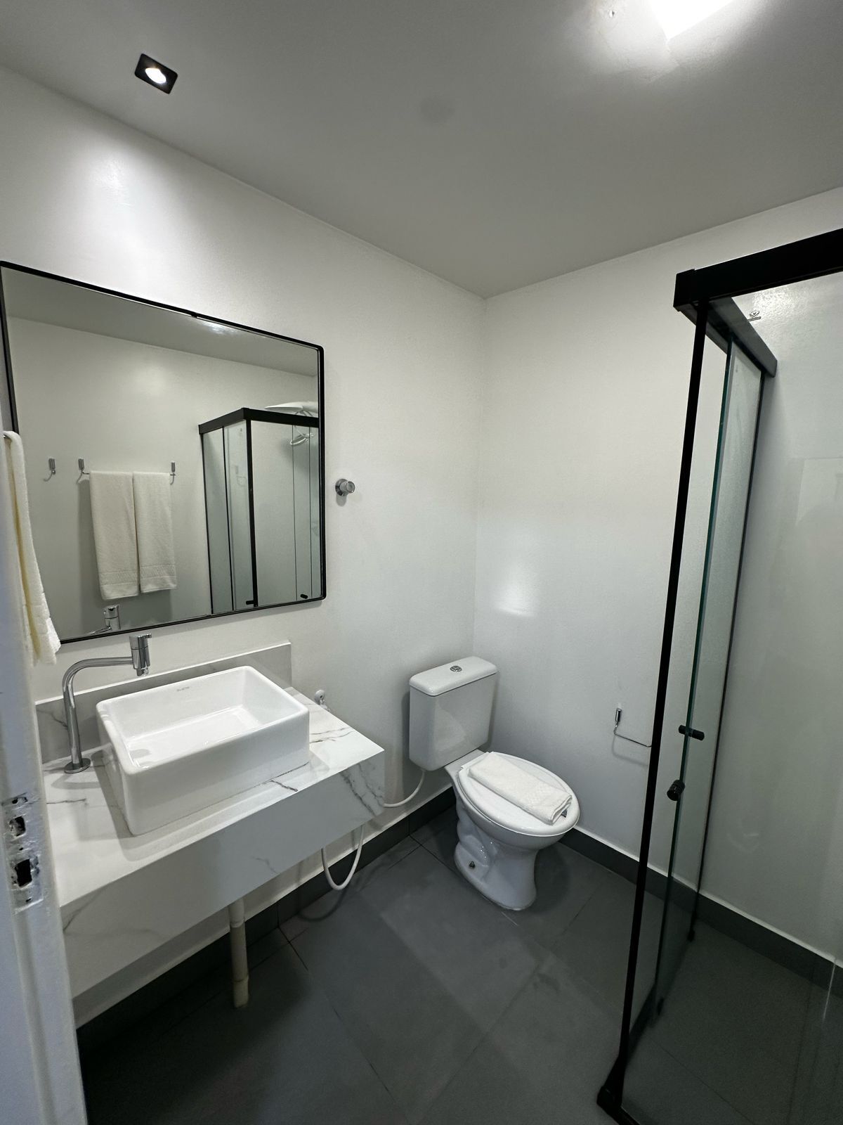 A modern bathroom with a white sink, mirror, toilet, and glass shower enclosure.