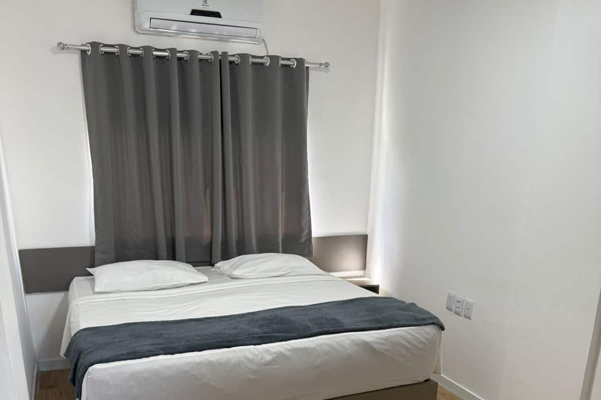 A bedroom with a bed, grey curtains, an air conditioning unit, and a wooden floor.
