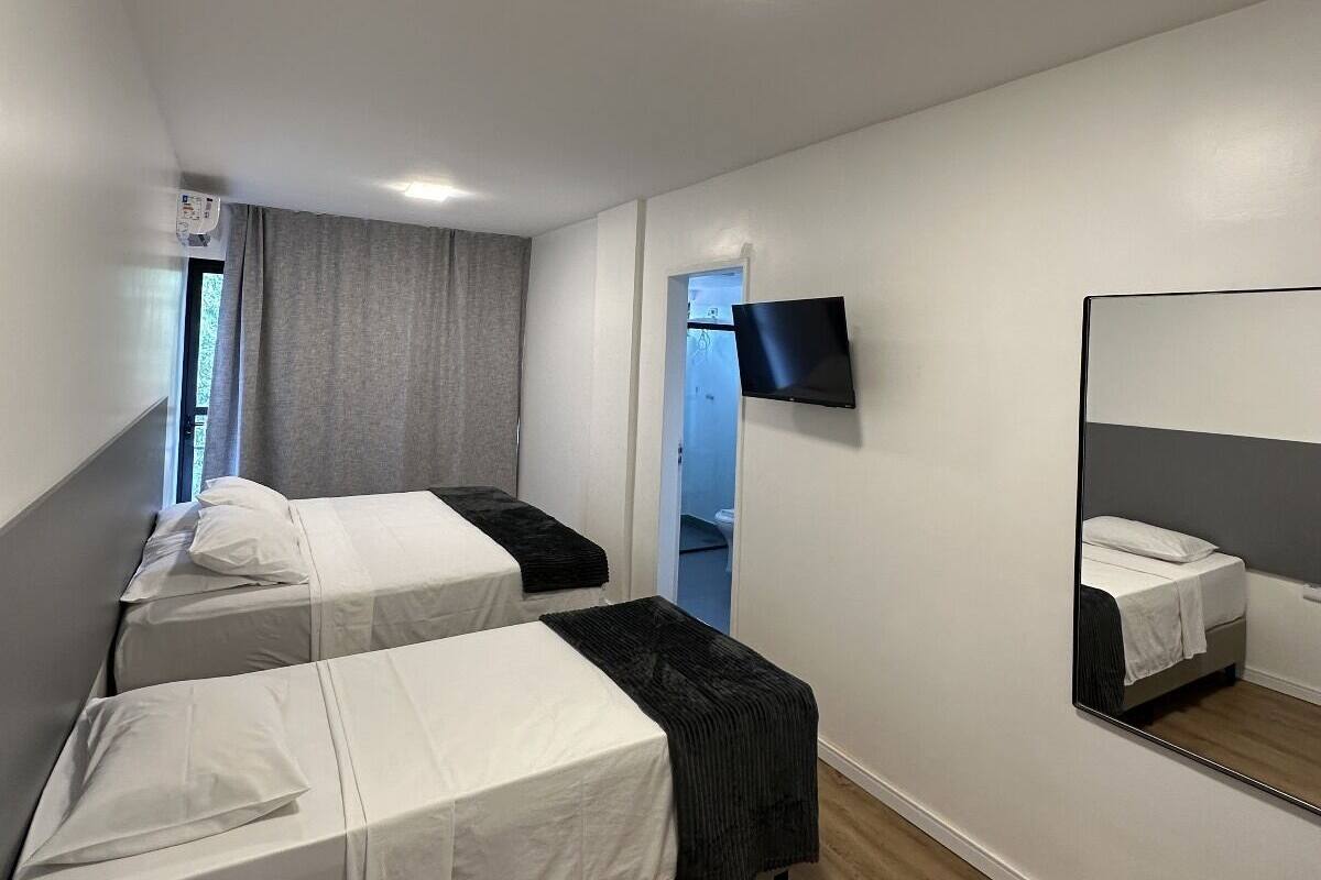A hotel room with two single beds, a flat-screen TV mounted on the wall, and a large mirror.
