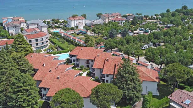 A coastal residential area with houses featuring red-tiled roofs, surrounded by greenery and a view of the sea. - Residence Sant Elena A19 by Wonderful Italy (Peschiera del Garda)