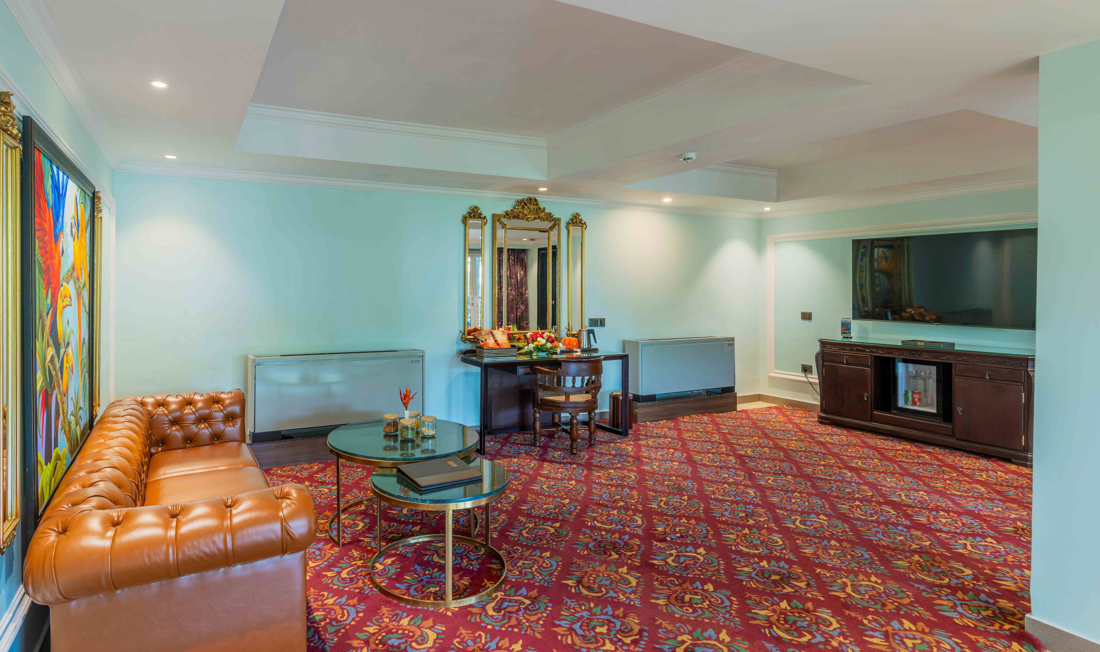 A spacious living room with a leather sofa, a glass coffee table, a decorative mirror, and a television.