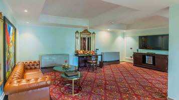 A spacious living room with a leather sofa, a glass coffee table, a decorative mirror, and a television.