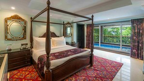 Una cama con dosel con un edredón rojo estampado, un espejo grande y ornamentado, y vistas a una piscina con azulejos azules desde un balcón.