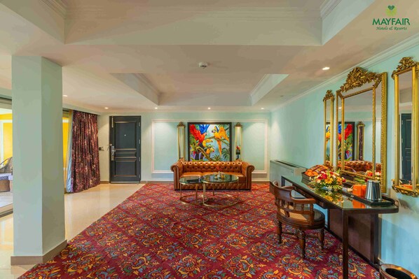 A hotel lobby with a patterned carpet, a sofa, a coffee table, and a desk with a mirror and flowers.