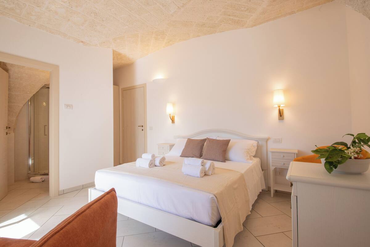 Ein Schlafzimmer mit Bett, Nachttischen, einem Sessel und einem Badezimmer mit Dusche und Toilette.