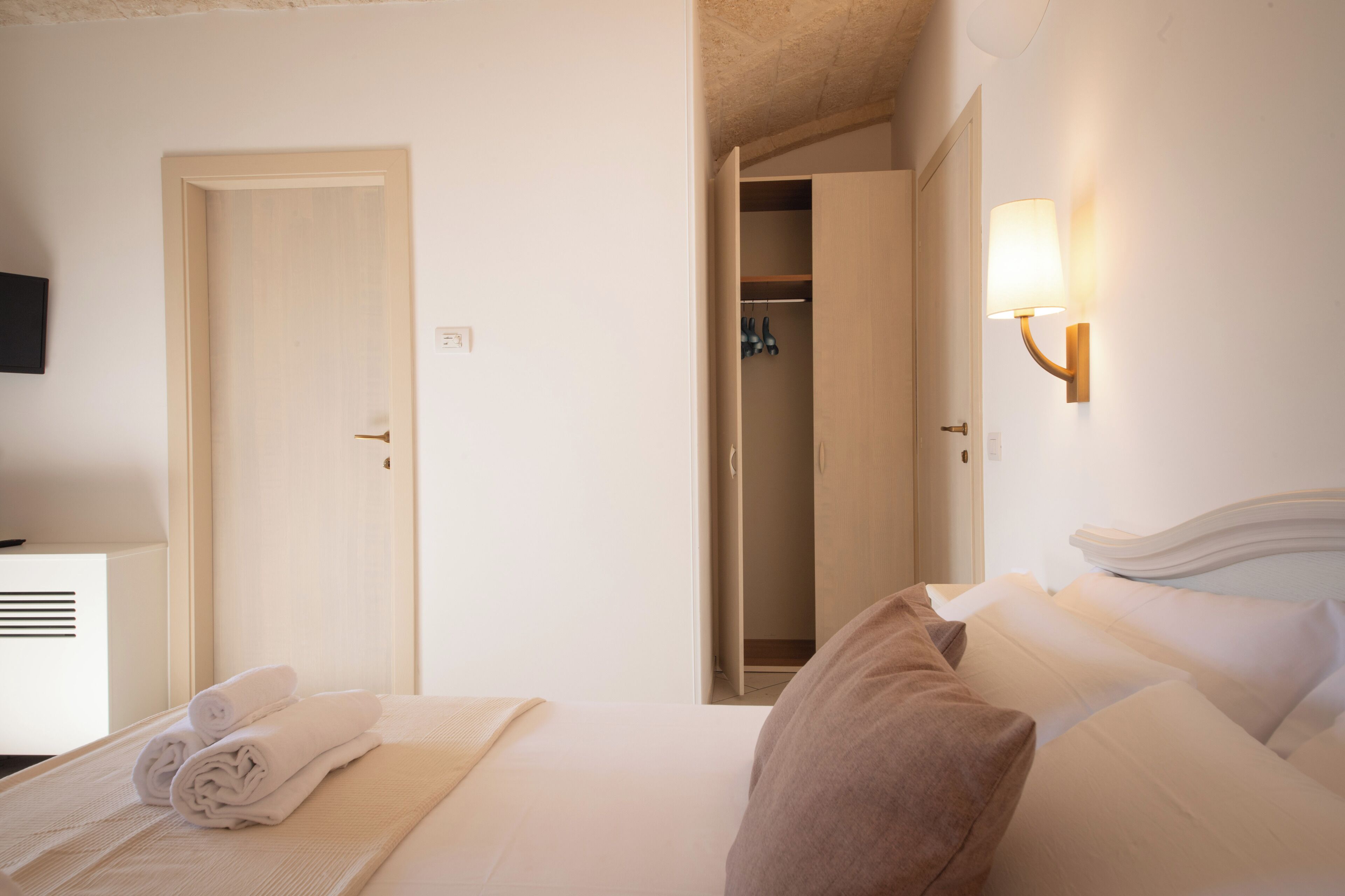 Een hotelkamer met een net opgemaakt bed, een gesloten deur en een zichtbare kast met hangende kleding.