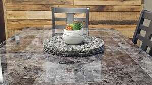 Une table à manger avec un plateau en marbre, entourée de chaises, et un panneau accroché au mur au-dessus.