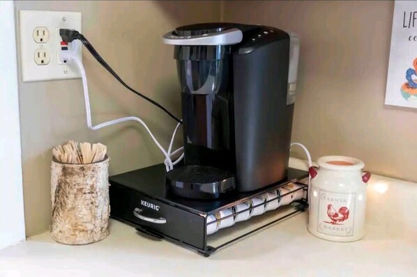 A Keurig coffee maker on a countertop with a coffee mug and a basket of newspapers.