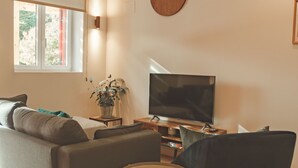 Moderni olohuone, jossa on sohva, nojatuoli, pieni pöytä, televisio ja seinällä oleva kello.