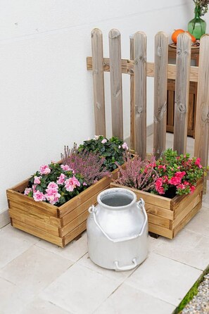 Deux jardinières en bois ornées de fleurs et un arrosoir en métal, le tout posé sur un sol carrelé.