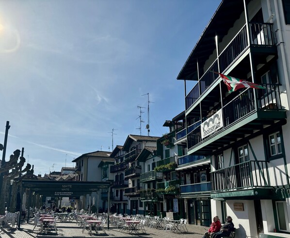Une rue avec des terrasses, des immeubles dotés de balcons et un ciel dégagé.