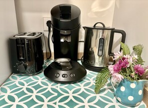 Une cuisine équipée d’un grille-pain, d’une machine à café, d’une bouilloire et d’un vase à fleurs posé sur une table à motifs.