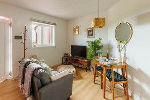 Ein Wohnzimmer mit einer Couch, Fernseher, einem Holzesstisch und einer Pflanze.