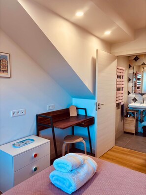 Ein Schlafzimmer mit Schreibtisch, Stuhl, Bett mit rosa Steppdecke und einem Badezimmer mit Spiegel und Waschbecken.
