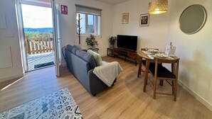 Un salon comprenant un canapé, un téléviseur, une table à manger et donnant sur l’extérieur grâce à une porte coulissante.