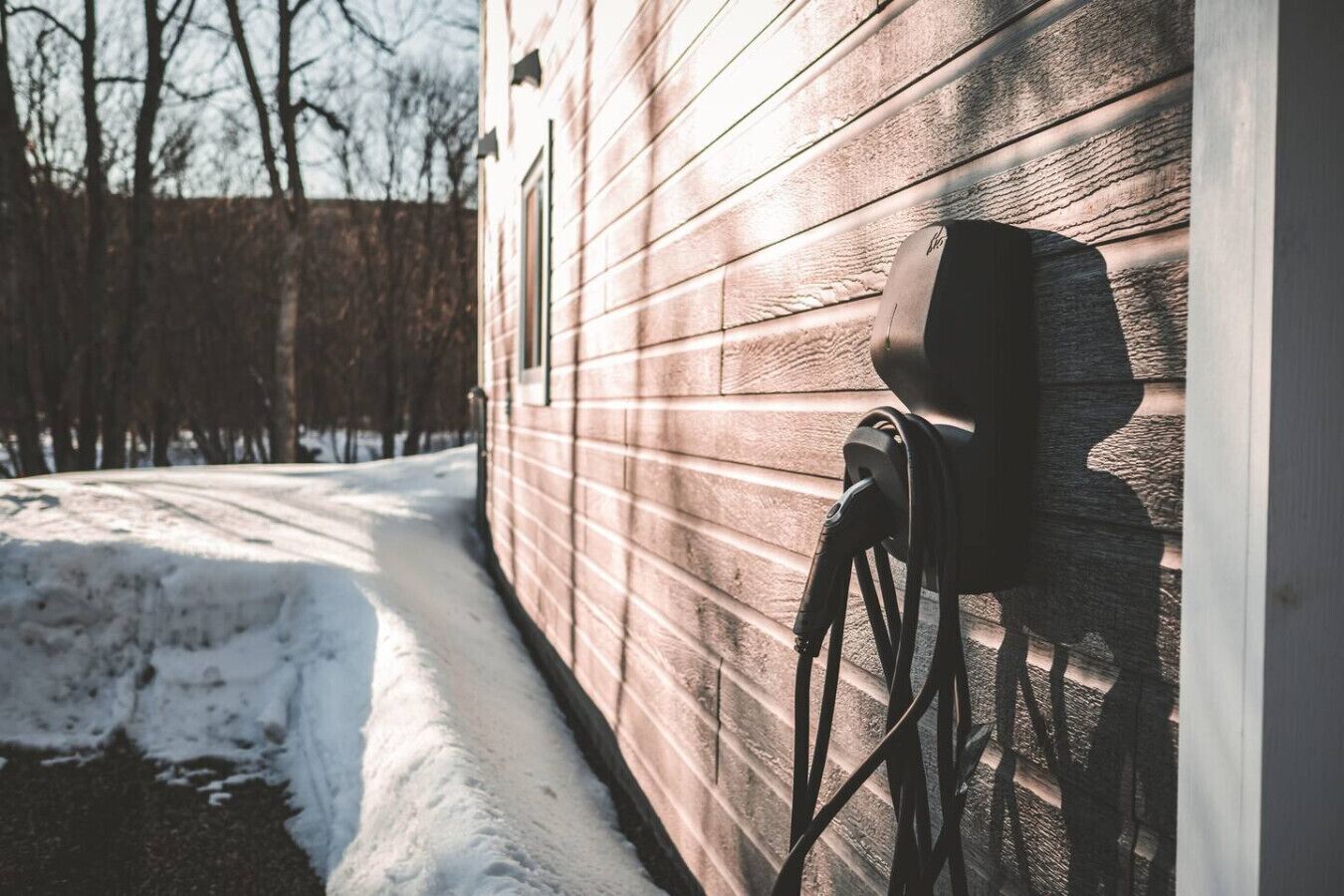 A snow-covered pathway leading to a wooden house with a solar panel mounted on the side.