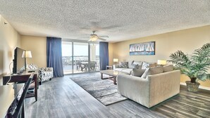 A spacious living room with a large window, a ceiling fan, a sofa, a coffee table, and a TV.