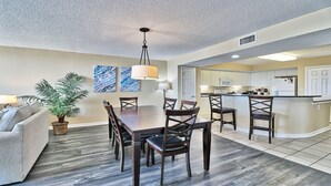 A modern kitchen with white cabinets, a central island, and a dining area with a wooden table and chairs.