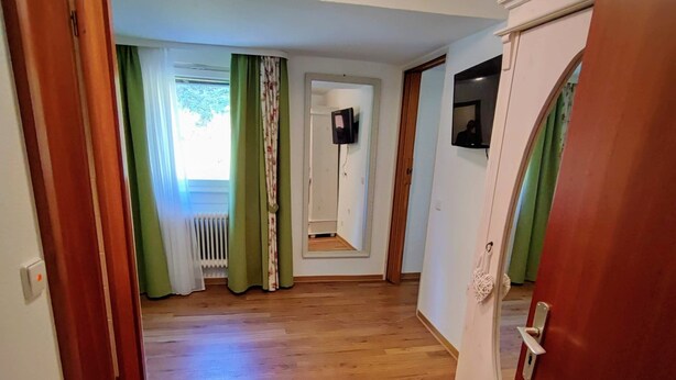 A hallway with wooden flooring, a door on the right, and a window with green curtains. - Room in Guest Room - Pension Forelle - Double Room n01 (Forbach)
