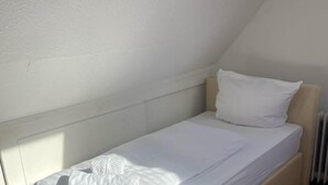 A small, single-bed room with white bedding and a wooden headboard. - Room in Guest Room - Pension Forelle - Double Room n01 (Forbach)