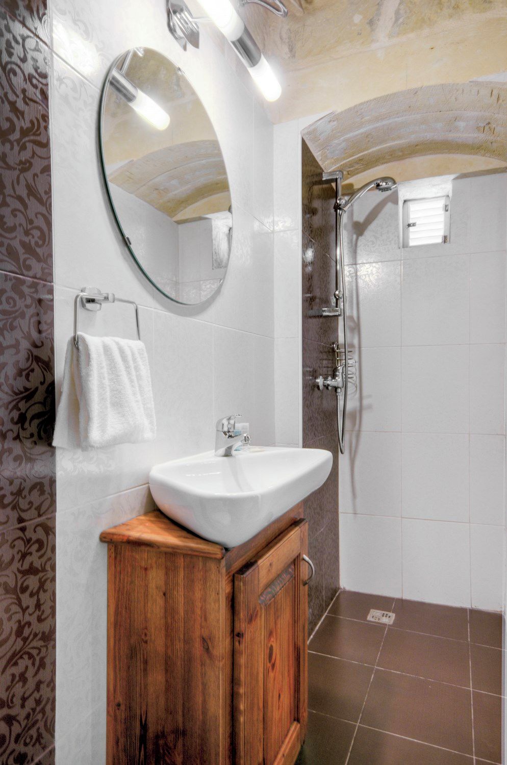 A bathroom with a white sink, wooden cabinet, mirror, and shower.
