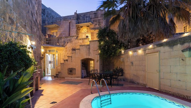 Una piscina con un muro de piedra y una puerta que da a un patio cubierto.