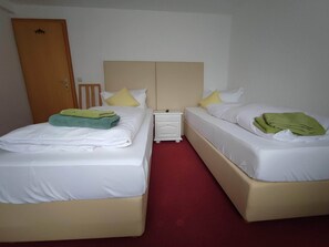 A hotel room with two beds, each with white linens and green towels. There is a wooden door and a white nightstand with a lamp. - Room in Guest Room - Pension Forelle - Double Room 01 (Forbach)
