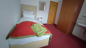 A hotel room with a bed, a bedside table, a wooden wardrobe, and a bathroom with a white sink. - Room in Guest Room - Comfortable Single Room With Shared Bathroom and Kitchen (Forbach)