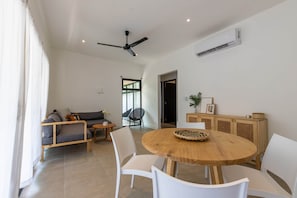 Uma sala de estar moderna com uma mesa de jantar de madeira, cadeiras brancas, um sofá cinza e um ventilador de teto.