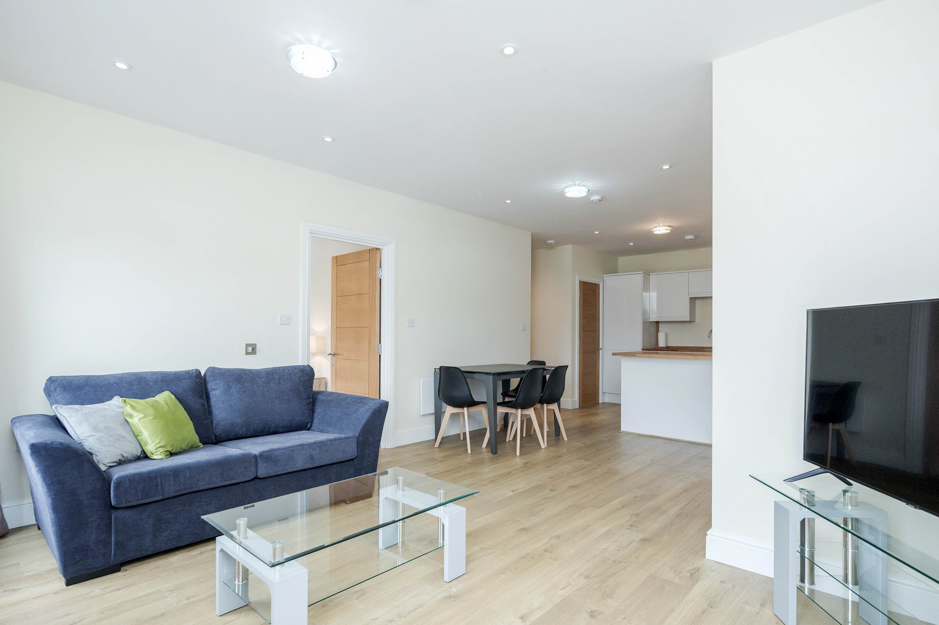 Una sala de estar moderna con un sofá azul, una mesa de centro de vidrio y un televisor sobre un mueble.