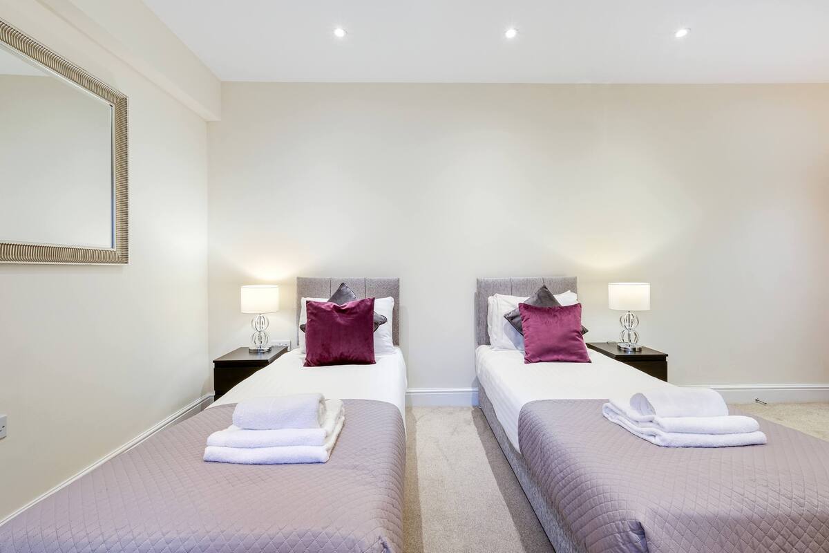 A hotel room with two beds, each with a pillow, a nightstand with a lamp, and a folded towel on the bed.