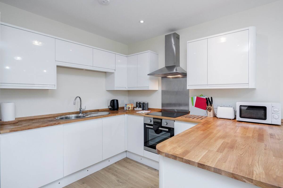 A modern kitchen with white cabinets, a stainless steel range hood, a microwave, and a wooden countertop.