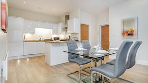 Una cocina moderna con armarios blancos, una isla central y una zona de comedor con mesa de vidrio y sillas grises.