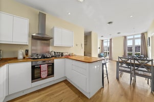 A modern kitchen with white cabinets, a stainless steel range hood, and a wooden countertop.