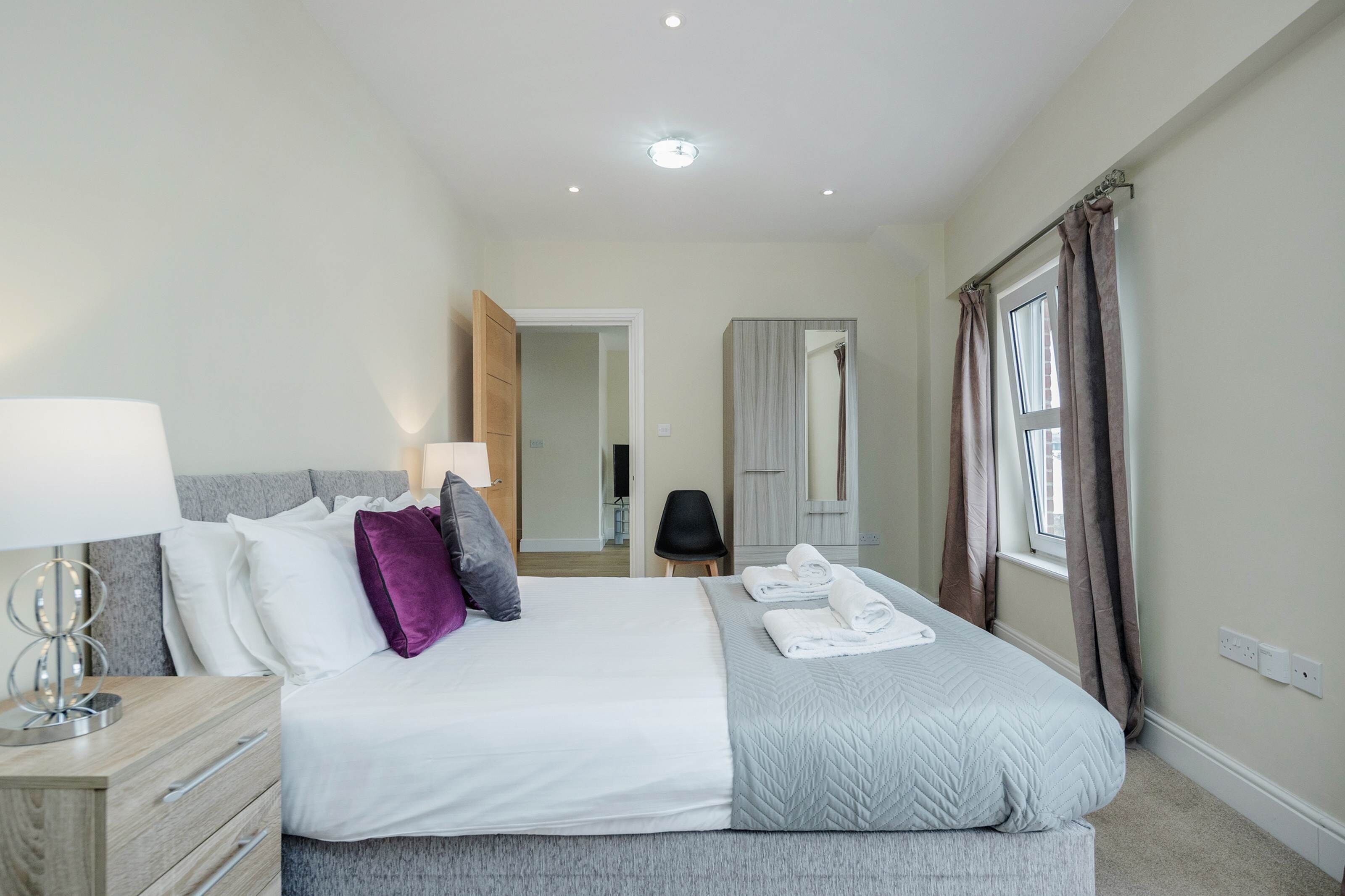 A hotel bedroom with a bed, bedside table, lamp, and a view of the bathroom.