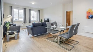 Una sala de estar moderna con una mesa de comedor de vidrio, sofás grises y un televisor de pantalla plana.