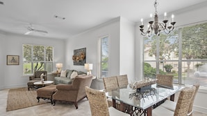 A dining area with a glass table and wicker chairs, a ceiling fan, and a chandelier.