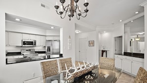 A modern kitchen with white cabinetry, stainless steel appliances, and a glass dining table.